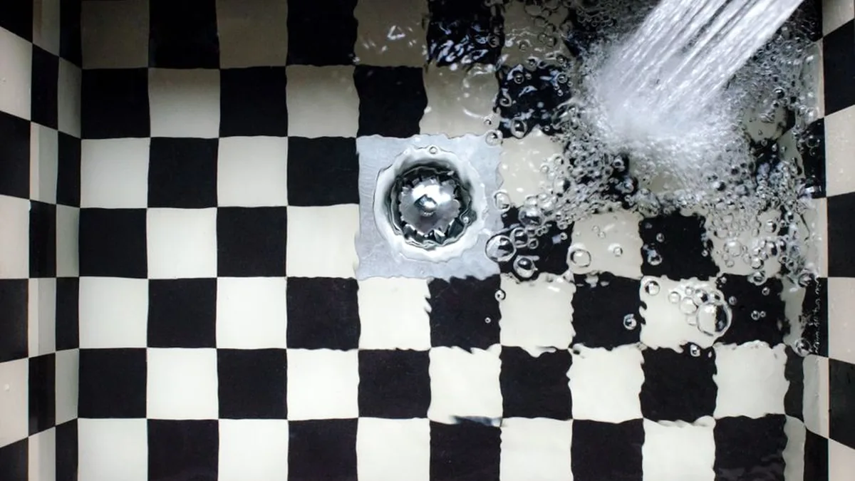 Water draining into the waste of a black and white tiled sink