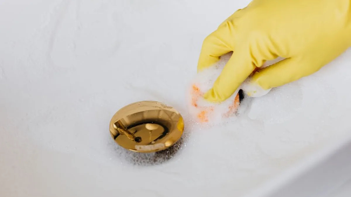 Gloved hand clearing debris from a basin waste outlet