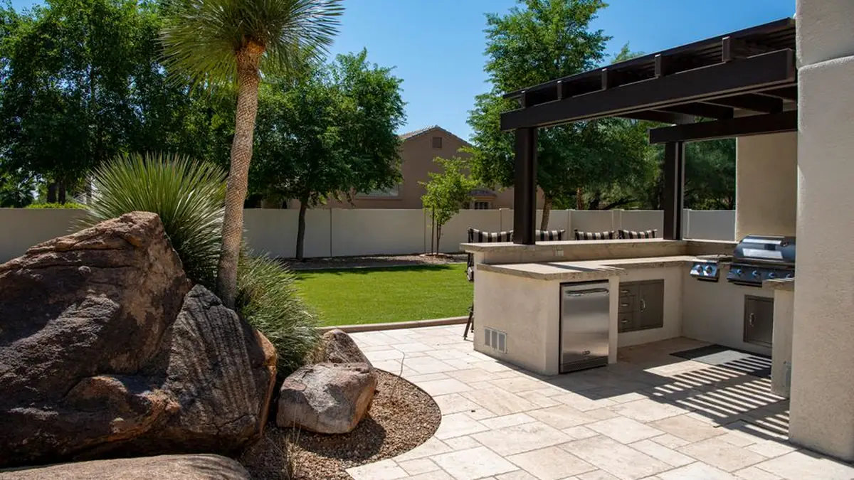 Landscaped backyard with large stone paving, a built-in outdoor kitchen under a pergola and mature planting
