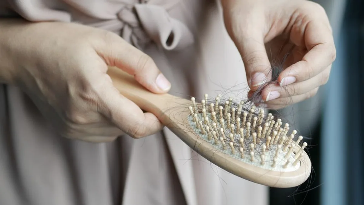 Two hands pulling a clump of loose hair off the bristles of a wooden hairbrush