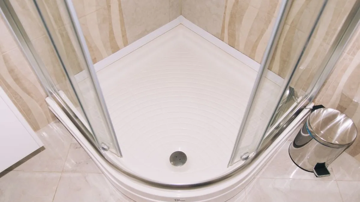 Chrome waste grate in the centre of a white corner shower base