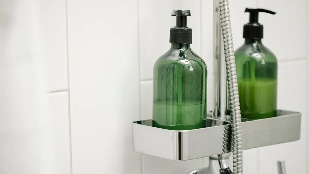 Two green pump bottles of body wash sitting in a chrome caddy on a white tiled shower wall