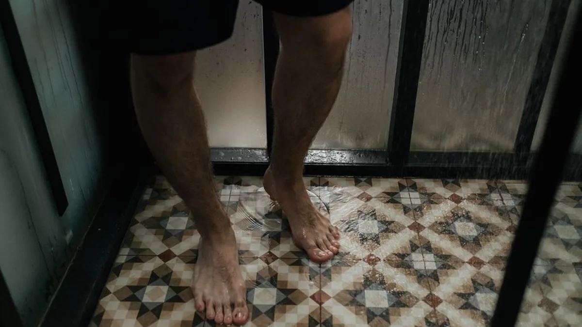 Bare feet standing on a wet patterned tiled bathroom floor with water spreading across it