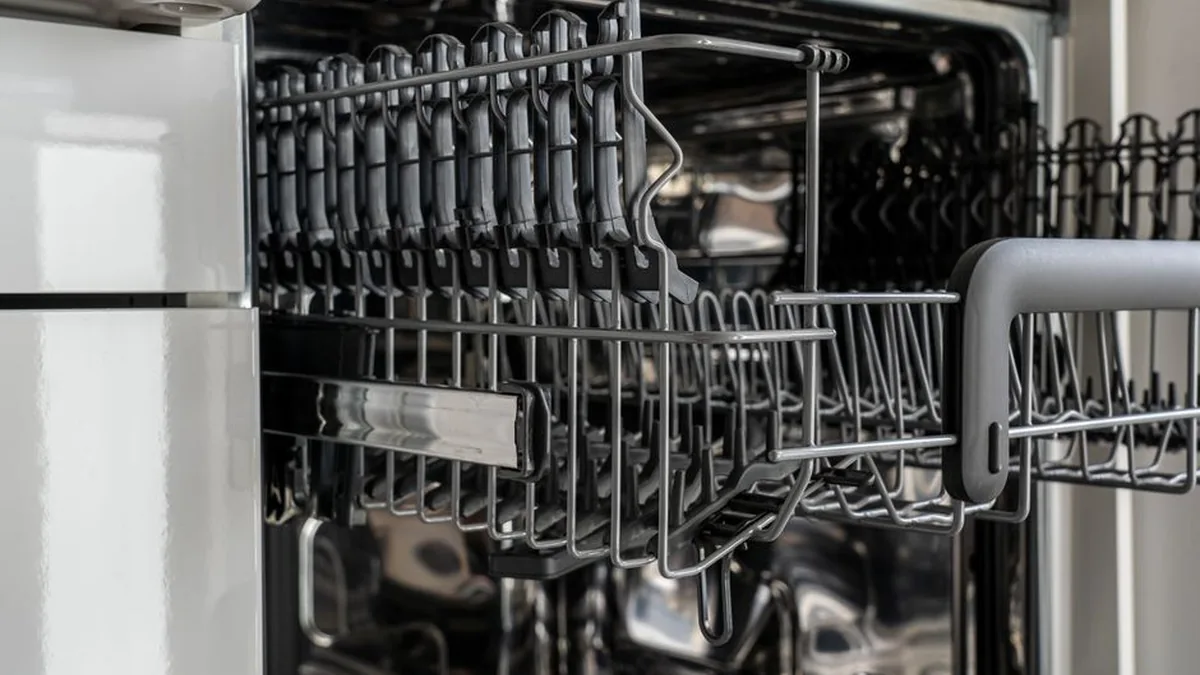 Open dishwasher door showing the empty upper and lower stainless steel racks and cutlery holder