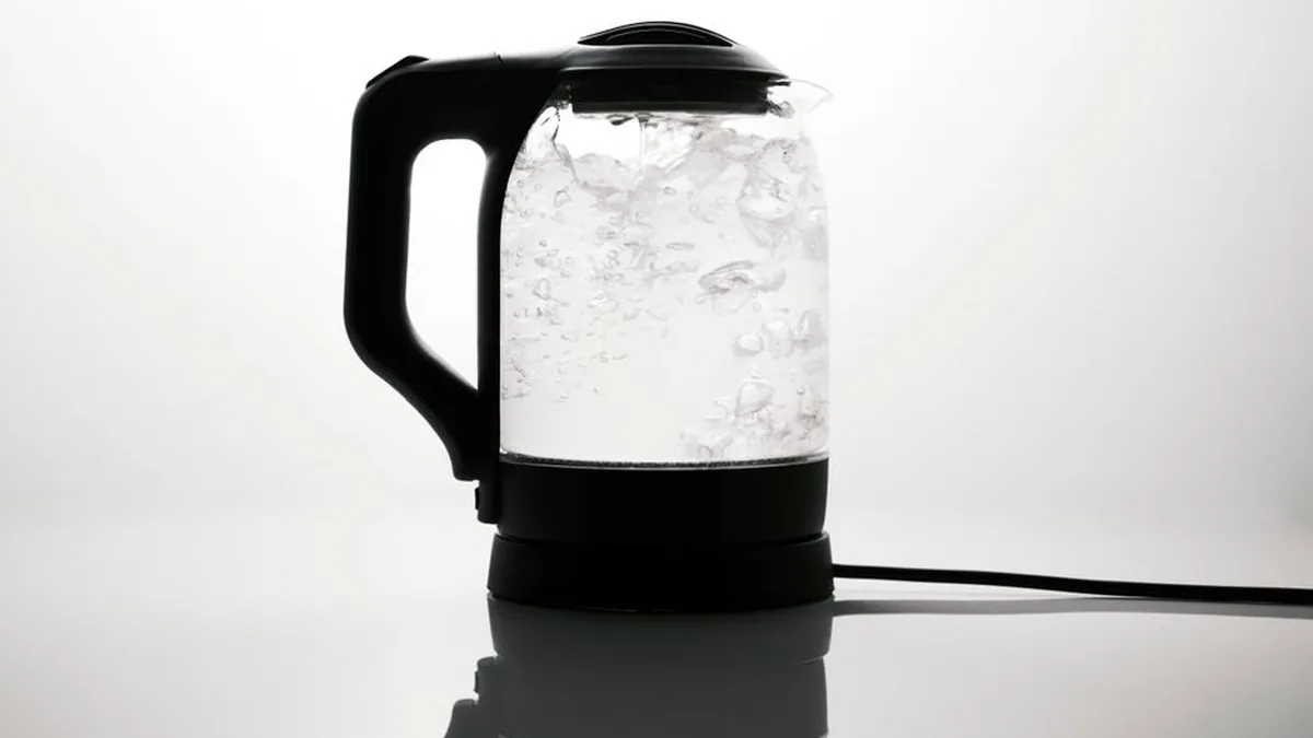 Glass electric kettle at a rolling boil on a plain white background