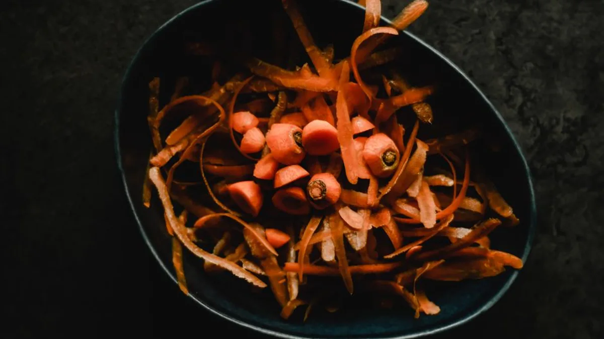 Overhead view of carrot peelings and trimmed carrot tops piled in a dark bowl on a slate surface
