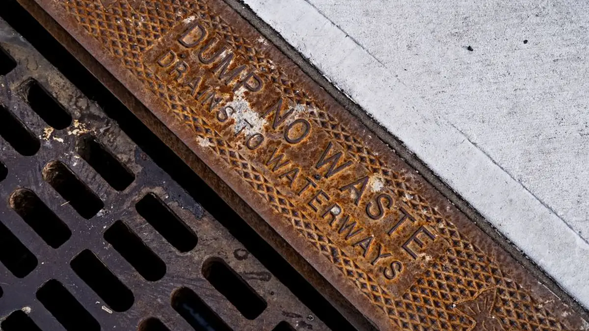 Rusted cast iron kerb grate with the words DUMP NO WASTE DRAINS TO WATERWAYS cast into its frame