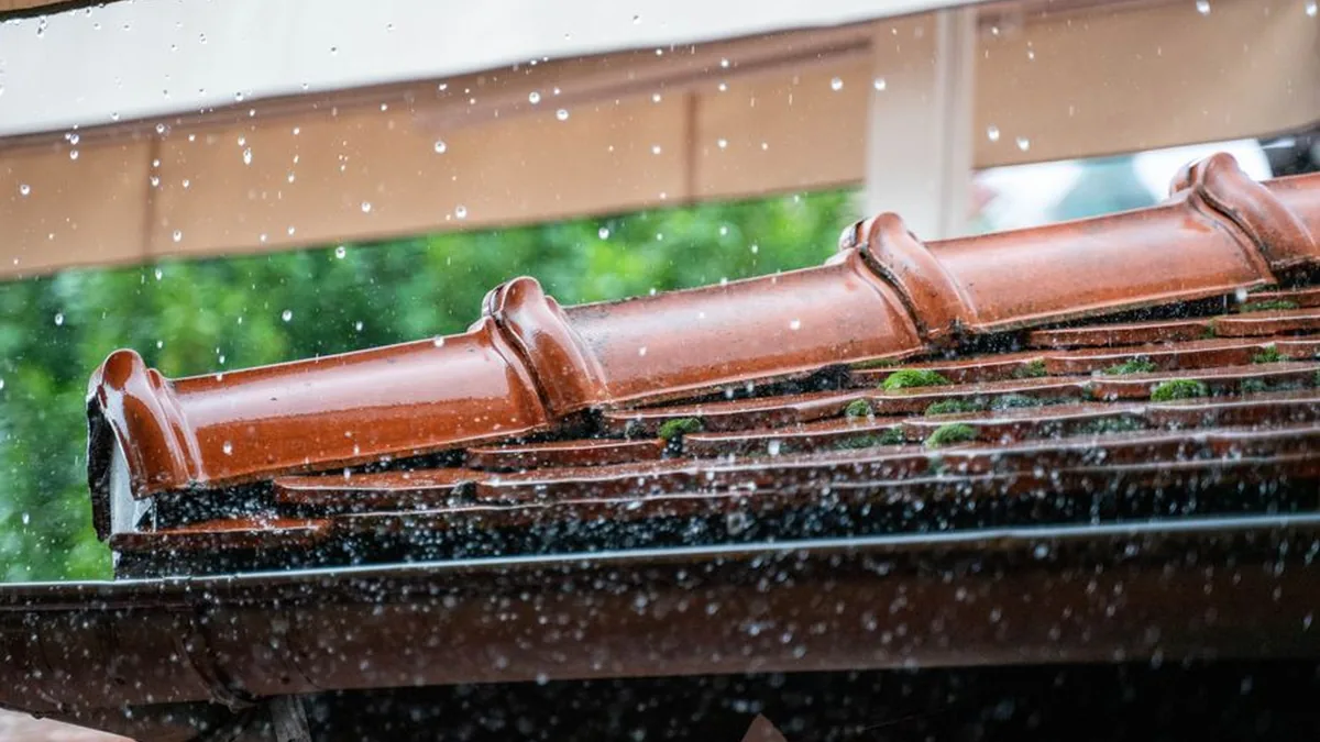 Rain falling into a terracotta half-round roof gutter and spilling over its front edge