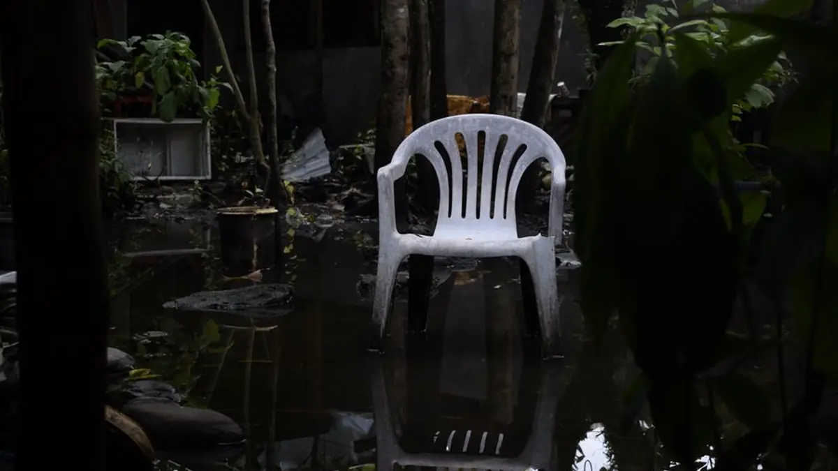 White plastic garden chair standing in several centimetres of water in a dark planted courtyard, reflected in the surface