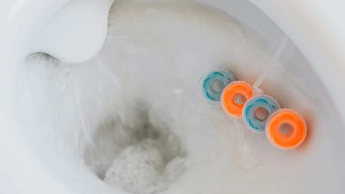 Water swirling through a white toilet bowl past a coloured plastic rim block clipped over the rim