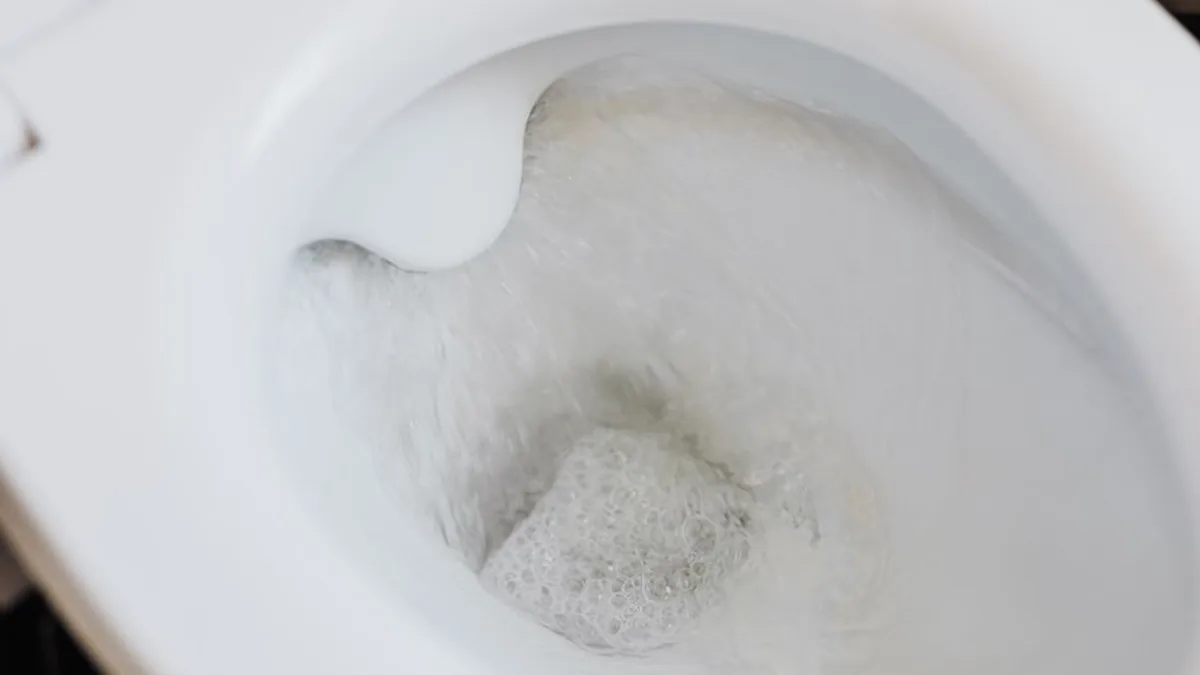 Water swirling down into the outlet of a white ceramic toilet bowl mid-flush