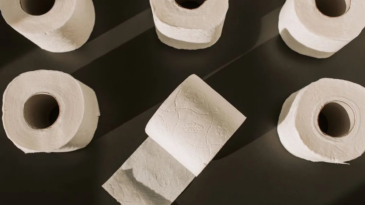 Six rolls of white toilet paper arranged on a dark grey surface with one sheet unrolled