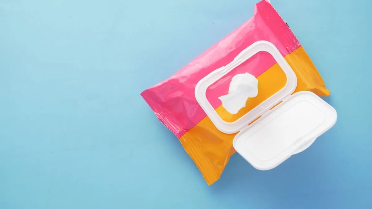 An opened pink and orange packet of wet wipes lying on a plain blue background